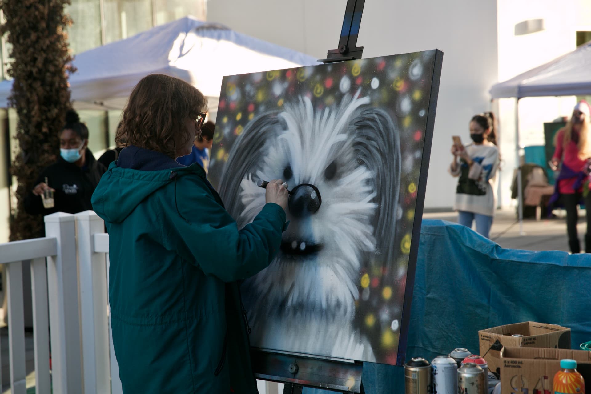 Artist spray-painting a portrait of a long-haired dog on canvas