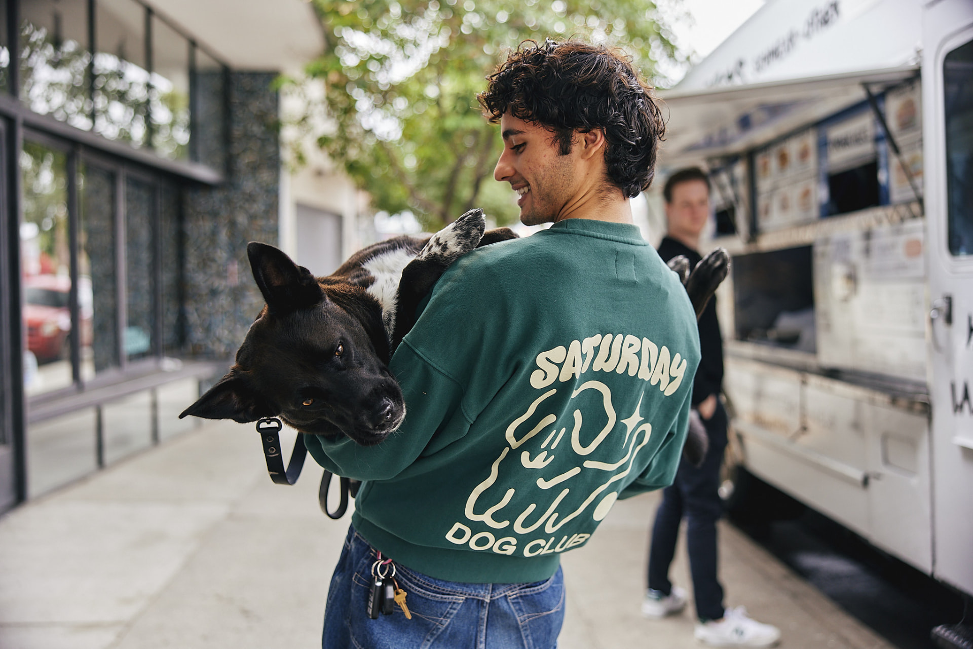 Dog parent in Saturday Dog Club sweatshirt carrying his dog