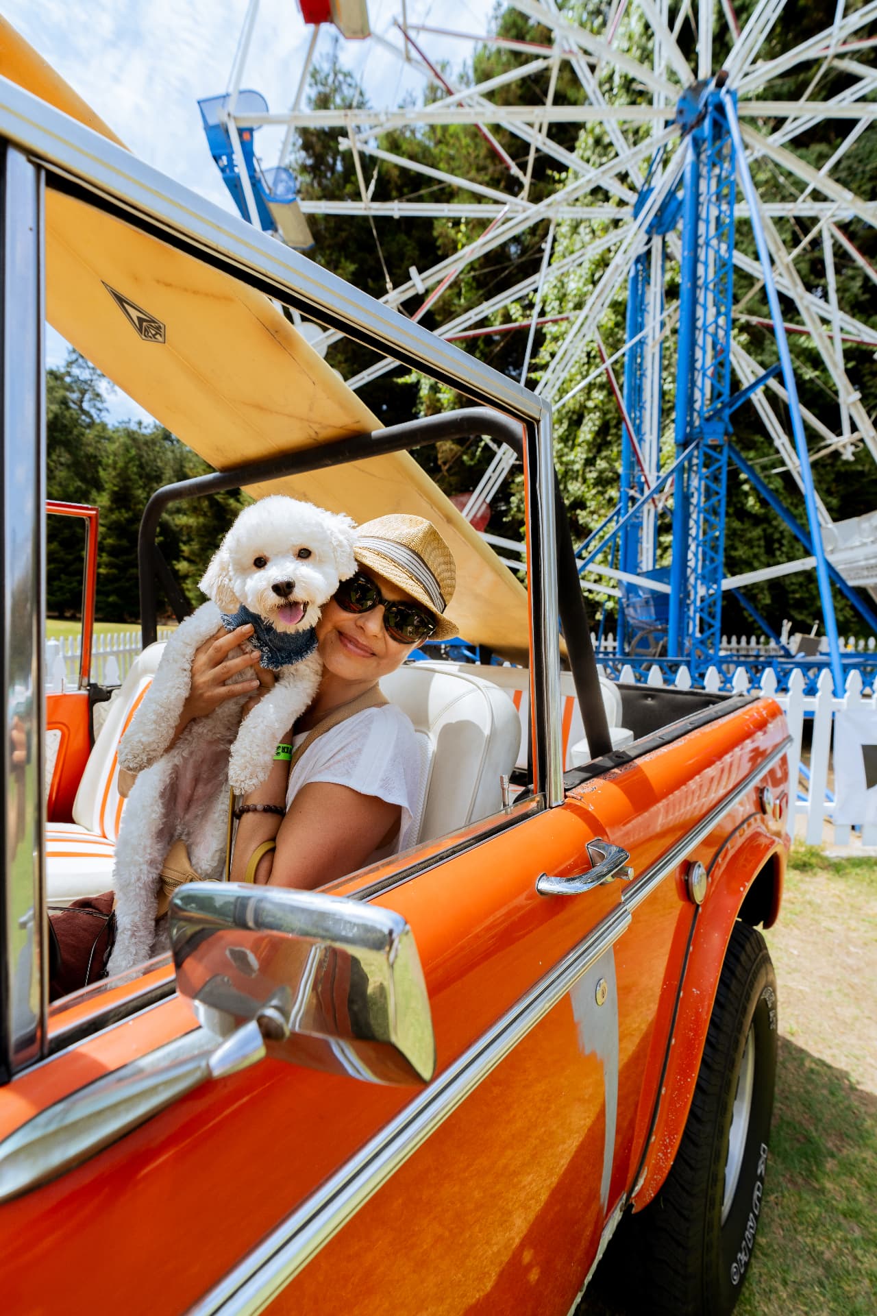 Woman with a small white dog inside a vintage orange truck by a ferris wheel