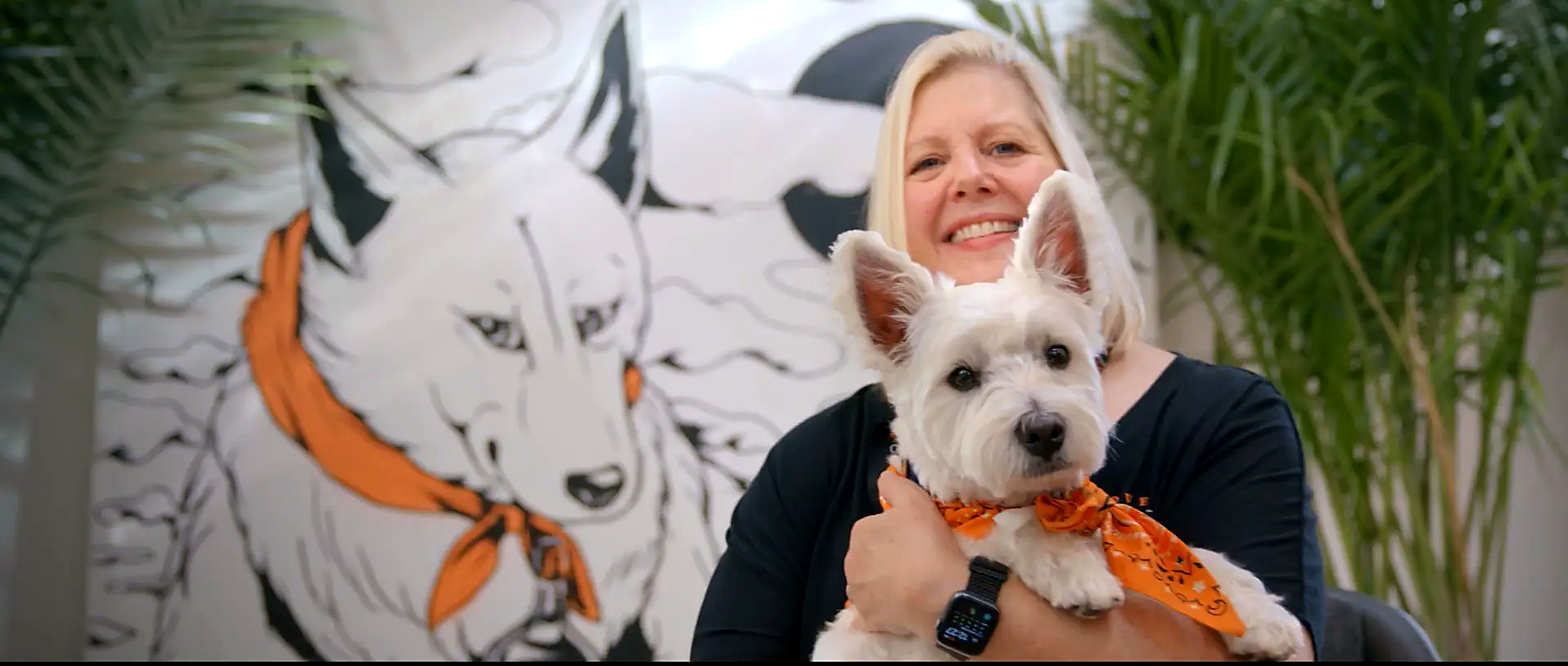 Tito's Handmade Vodka employee holding her westie in front of a mural