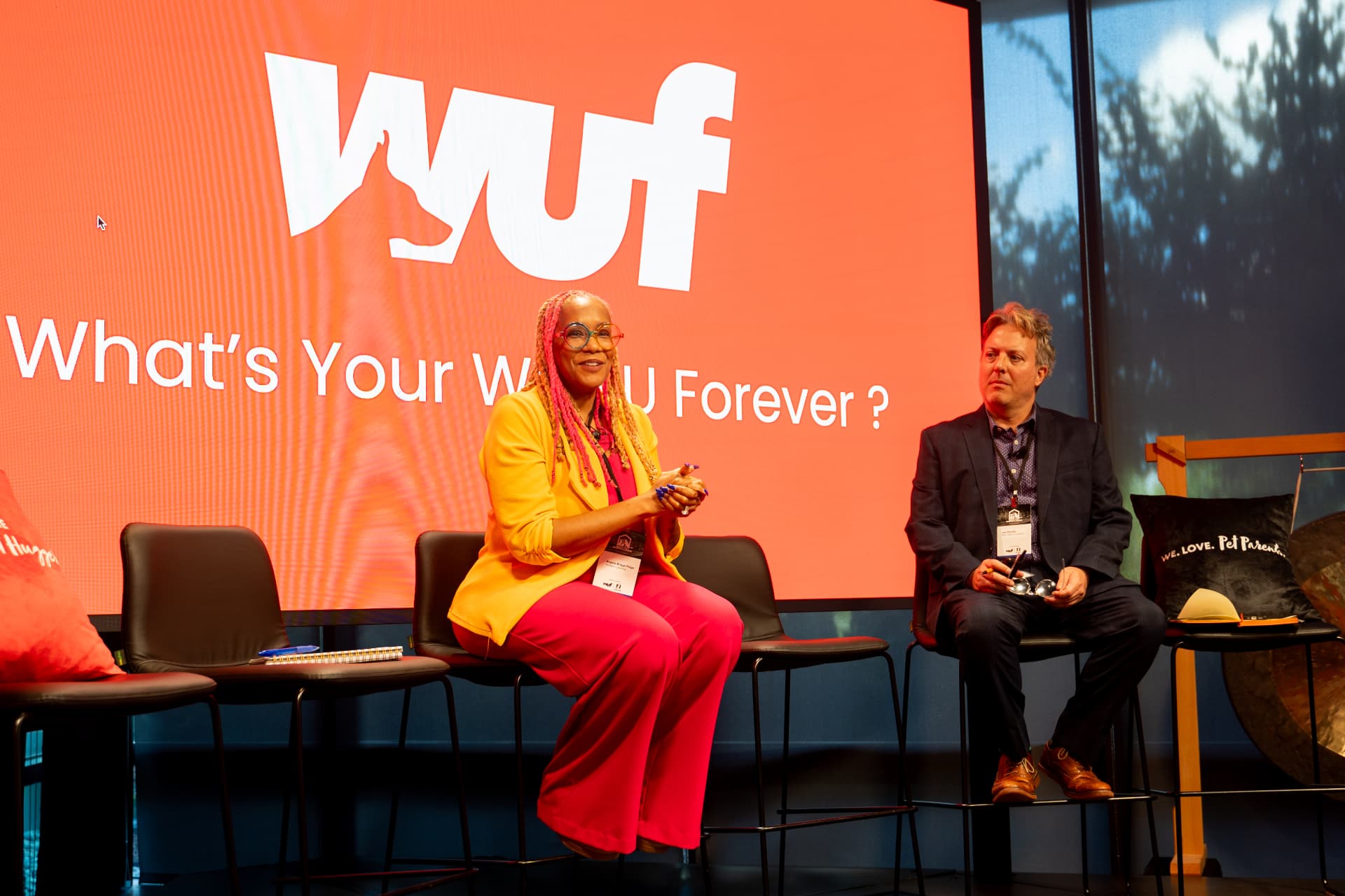 Two panelists on stools in front of a 'What's Your WUF Forever?' screen